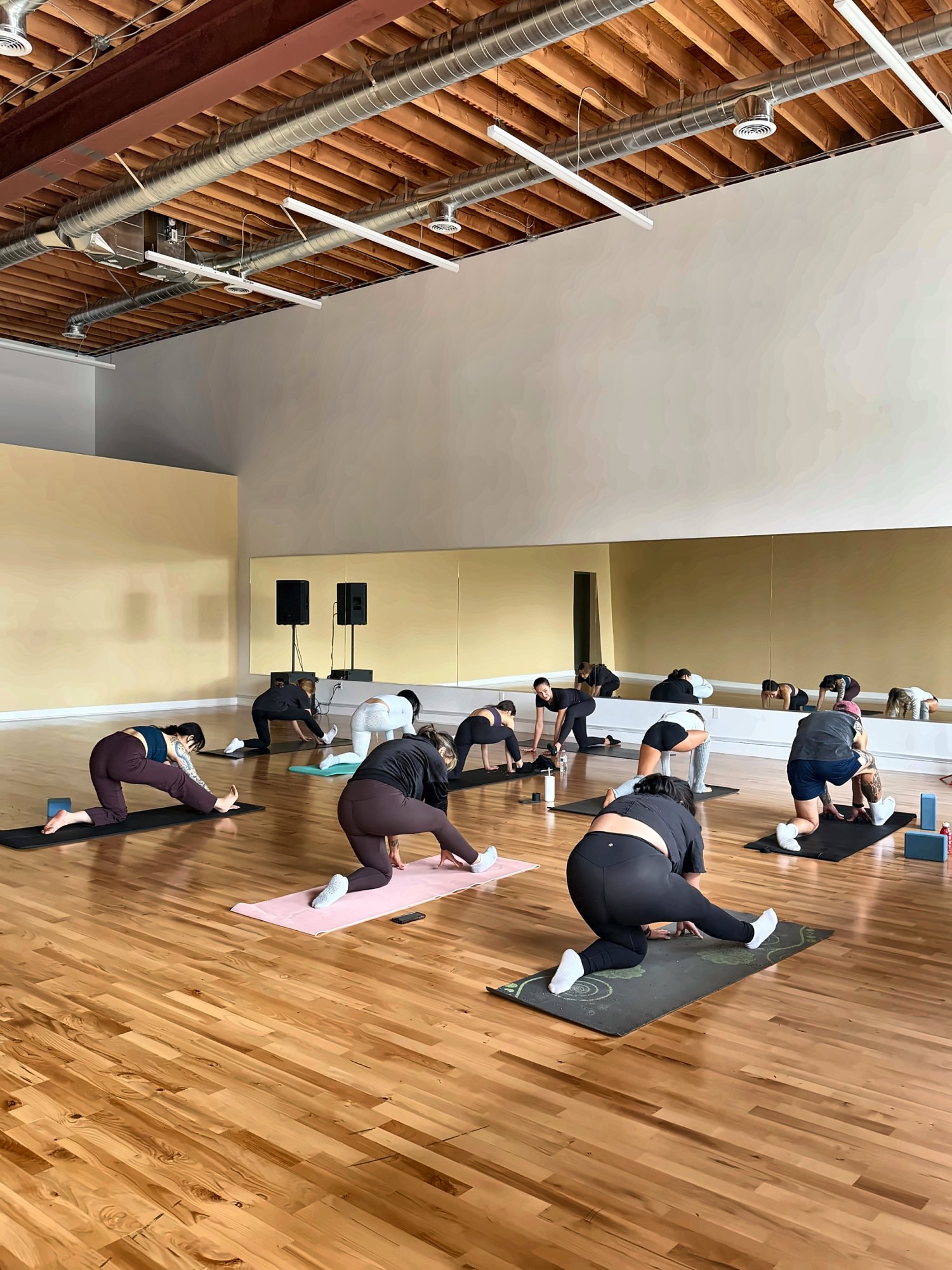Stretching class on mats in the main studio with wood-beam ceiling